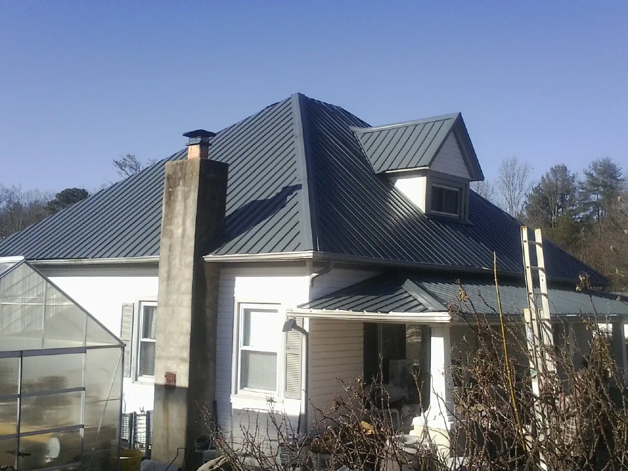 Dark blue standing seam metal roof on a white farmhouse with dormer — Slate & Tile Roof Repair by Roofing Brothers in Ama