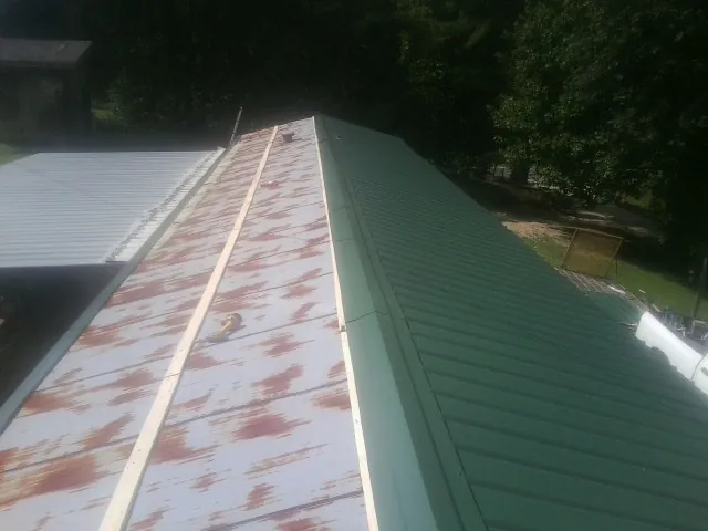 Old rusted panels beside newly installed green metal roofing — Wind Damage Roof Repair by Roofing Brothers in Ama