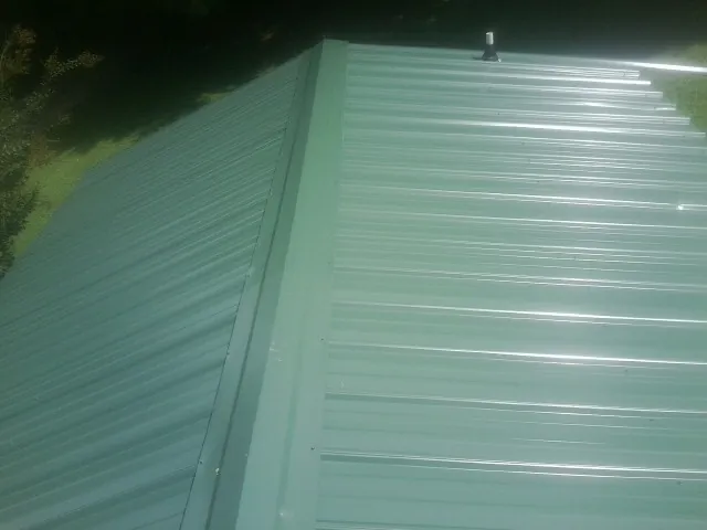 New green metal panels meeting at the ridge of a roof — Flat Roof Repair work by our crew in Ama