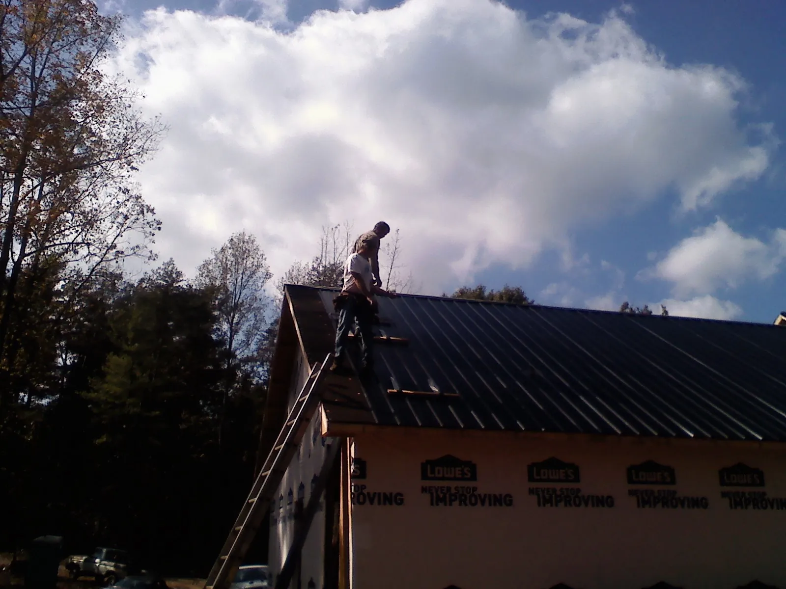Roofer fastening dark metal panels high against a cloudy sky, from a Roof Inspection job in Ama